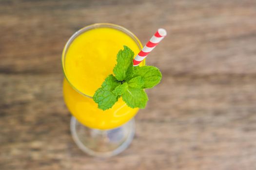 Juicy smoothie from mango in glass with striped red straw and with a mint leaf on old wooden background. Healthy life concept, copy space.