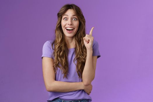 Excited cheerful happy creative smart girl raise index finger eureka gesture smiling broadly stare camera thrilled got excellent idea share suggestion think up perfect solution purple background. Lifestyle.