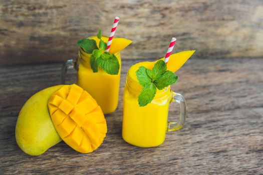 Juicy smoothie from mango in two glass mason jars with striped red straw on old wooden background. Healthy life concept, copy space.