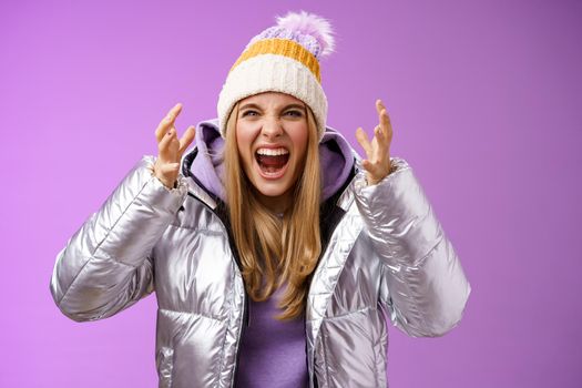 Outraged fed up pissed blond woman screaming out loud hateful bending forward shaking hands disrespect angry arguing heartbroken cry standing bothered quarreling, purple background.