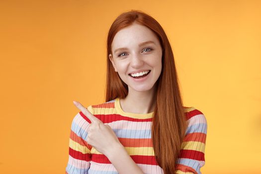 Friendly outgoing good-looking ginger girl university student discussing lecture classmate smiling laughing pointing upper left corner questioned curious know details standing orange background.