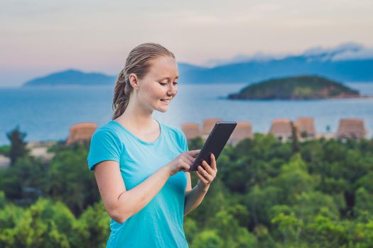 Young woman enjoys a tablet on the background of the sea.