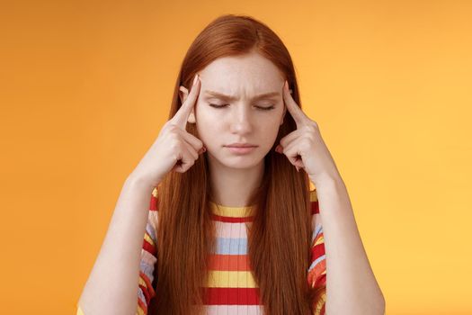 Girl getting thoughts piled trying think stright focusing concentrating important task remember number touch temples close eyes look seriously standing puzzled suffer headache, orange background.