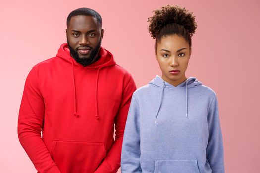 Two cute african american siblings standing together pink background invited family dinner greet new mom boyfriend, sister look displeased serious brother smug have idea prank stepdad.