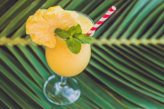 Pineapple and pineapple smoothies against the background of a branch of a palm tree.