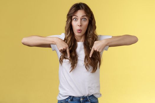 You see that too. Surprised wondered amazed happy astonished funny cheerful girl long curly haircut stare impressed amazed pointing down react fascinated curious bottom promo yellow background.