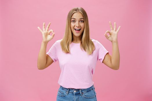 Portrait of enthusiastic attractive caucasian girl in trendy t-shirt and jeans showing okay or confirm gesture with amused broad smile standing pleased over pink background reacting to excellent news. Lifestyle.