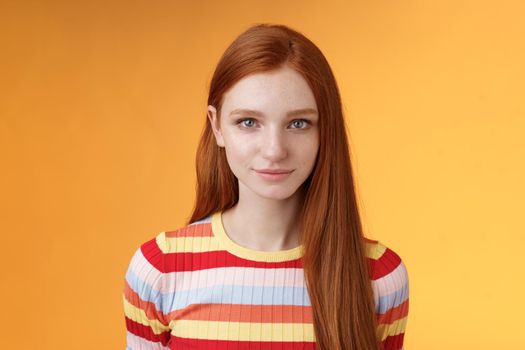 Attractive young sincere redhead girl clean pure perfect skintone smiling modest look camera friendly delighted standing relaxed awaiting gazing silly tenderly, posing orange background. Copy space