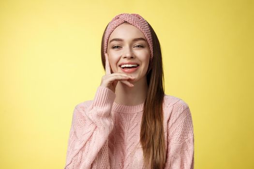 Cheerful entertained young attractive european woman in knitted pink headband, sweater touching cheek smiling, laughing. Student with smile on face, having fun, giggling over comedy movie.