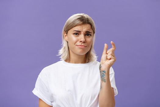 Woman feeling regret lacking small amount of money to afford car. Unhappy displeased good-looking stylish female with tattoos on hands frowning and pursing lips shaping tiny or little object.