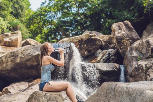 Young woman drinks water on a waterfall background.