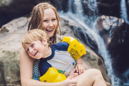 Mom and young son on the waterfall background. Traveling with kids concept.