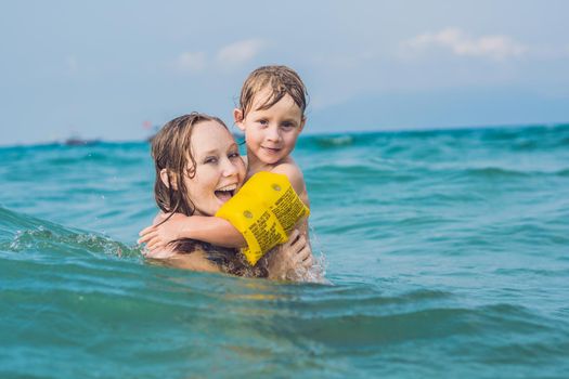 Young mother swimming and playing with male child boy in sea or ocean water sunny day outdoor on natural background, horizontal picture.