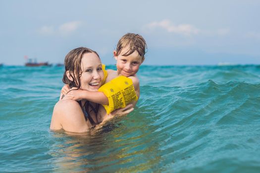 Young mother swimming and playing with male child boy in sea or ocean water sunny day outdoor on natural background, horizontal picture.