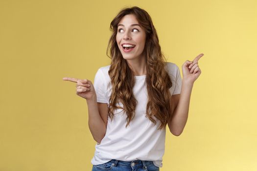 Amused cheerful smiling happy young curly-haired woman chestnut hair observe curiously copy space grinning admiration joy pointing sideways making choice impressed satisfied turn left.