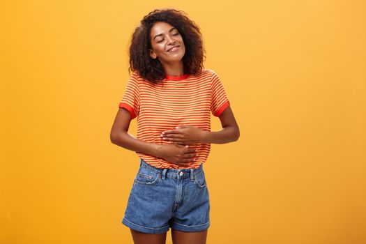 Mmm delicious meal warming me inside. Delighted stuffed good-looking stylish young female in striped t-shirt rubbing belly with satisfaction closing eyes from pleasure after eating tasty food. Restaurants and people feelings concept