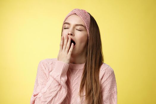 Time to bed. Portrait of tired cute sleepy girlfriend wearing sweater, knitted headband yawning cute with closed eyes opened mouth covered with palm, exhausted, wanting sleep, dreaming fall asleep.