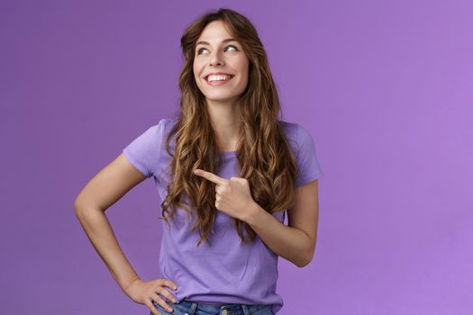 Cheerful motivated enthusiastic upbeat curly-haired girl turn left pointing sideways contemplate produly good choice smiling delighted having perfect summer day stand purple background.