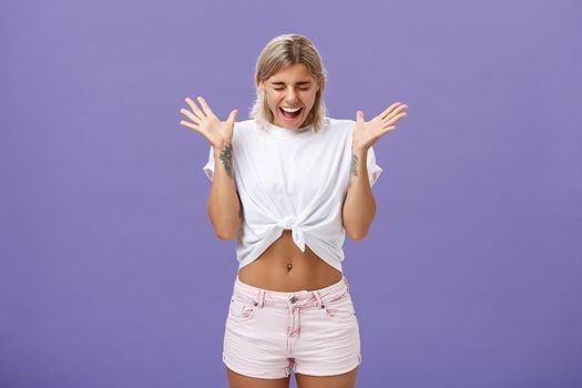 Studio shot of woman having mental breakdown screaming out loud shaking raised palms closing eyes and bending head down feeling scared and yelling from fear over purple background. Emotions concept