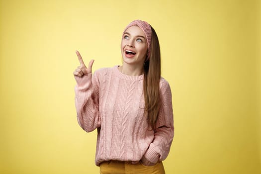 Amused and impressed dreamy pretty young european woman in knitted sweater gasping entertained dropping jaw smiling thrilled, joyful, pointing, looking at upper left corner excited of awesome promo.