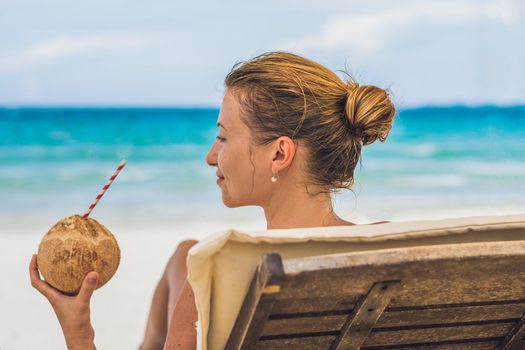 Young woman drinking coconut milk on Chaise-longue on beach. Dream scape Escape with beauty girl. The Benefits of Coconut Water.