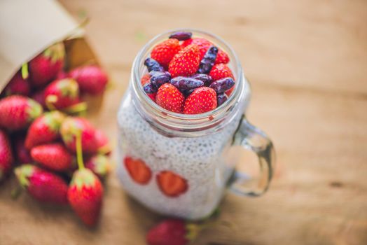 Healthy layered dessert with chia pudding, strawberry and honeysuckle in a mason jar on rustic background.