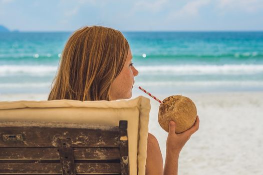 Young woman drinking coconut milk on Chaise-longue on beach. Dream scape Escape with beauty girl. The Benefits of Coconut Water.