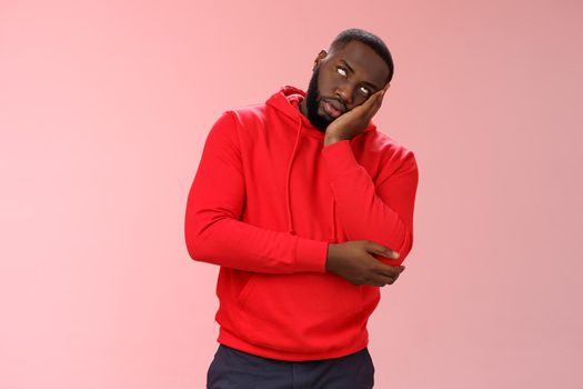 Annoyed bored funny attractive african american guy in red hoodie roll eyelids facepalm head lean hand, hear stupid uninteresting story dying boredom, standing careless rude pink background.