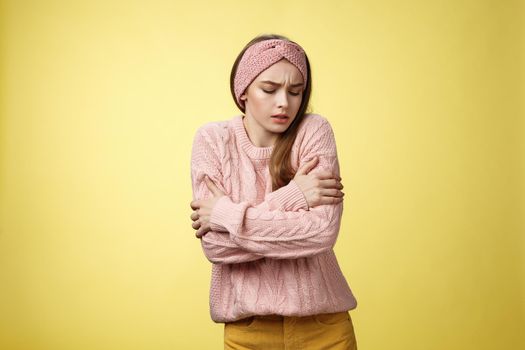 Brr girl freezing, turn-on heater. Portrait of timid cute woman wearing knitted sweater trembling from cold, embracing herself on arms looking down, stooping from discomfort cool temprature.