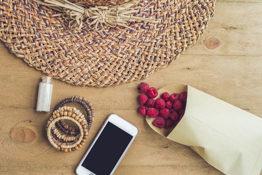 Summer holiday, vacation, relaxation concept. Raspberries, straw hat, mobile phone, smartphone, headphones, sunglasses from above, top view, flat lay on wooden background. Colorful background with free text copy space. Summer vibes concept.