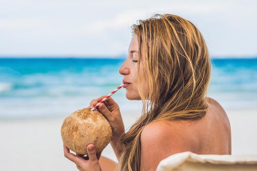 Young woman drinking coconut milk on Chaise-longue on beach. Dream scape Escape with beauty girl. The Benefits of Coconut Water.