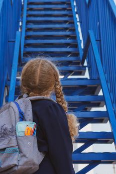 Schoolgirl looking up the stairs.. Concept  school days, start date, next stage, career ladder, the beginning of the way. girl in a uniform with a backpack. Girl near the stairs.