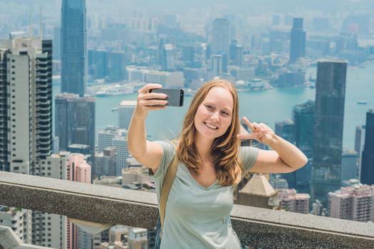 Hong Kong Victoria Peak woman taking selfie stick picture photo with smartphone enjoying view over Victoria Harbour. Viewing platform on top of Peak Tower, HK. Defocused background.Travel asia concept.