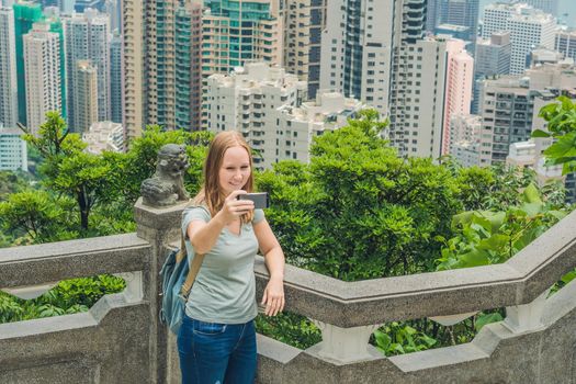 Hong Kong Victoria Peak woman taking selfie stick picture photo with smartphone enjoying view over Victoria Harbour. Viewing platform on top of Peak Tower, HK. Defocused background.Travel asia concept.