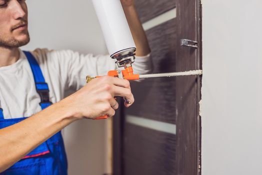 Young handyman installing door with an mounting foam in a room.