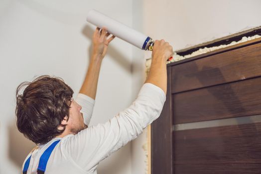 Young handyman installing door with an mounting foam in a room.