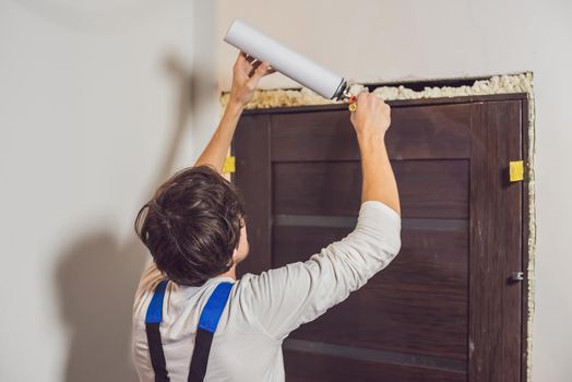 Young handyman installing door with an mounting foam in a room.