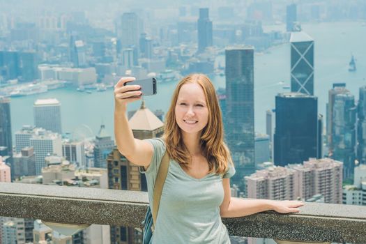 Hong Kong Victoria Peak woman taking selfie stick picture photo with smartphone enjoying view over Victoria Harbour. Viewing platform on top of Peak Tower, HK. Defocused background.Travel asia concept.