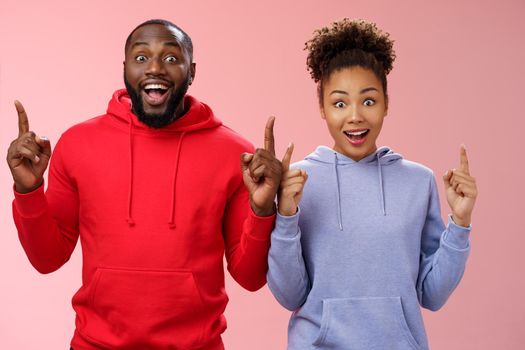 Amused charismatic two best friends african american brother sister pointing raised index fingers up widen eyes imressed amused feel happy go study abroad together winning trip standing surprised.