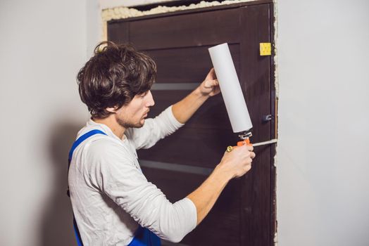 Young handyman installing door with an mounting foam in a room.