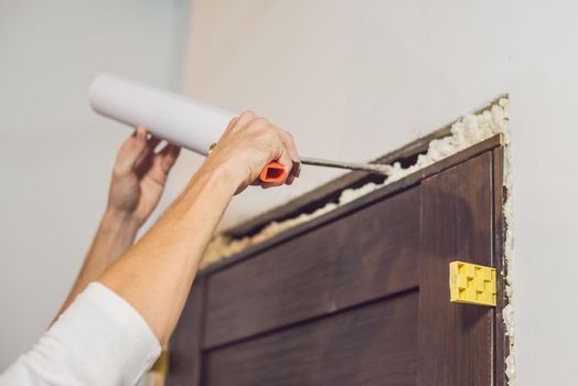 Young handyman installing door with an mounting foam in a room.