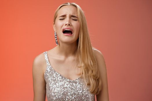 Immature whining spoiled adult rich daughter blond long hair in silver stylish dress complaining sad cruel unfair life crying sobbing frowning sulking upset, standing disappointed red background.