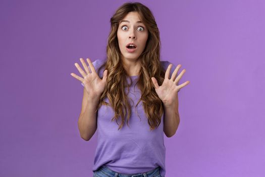 Ambushed shocked girl gasping not expect friend jump out corner raise palms surprised astonished drop jaw open mouth stunned stare camera impressed stupefied purple background. Copy space