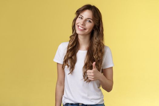 Well done congratulations. Happy charismatic pretty european female tilt head smiling broadly accept agree your idea like satisfied good result show thumb up approval gesture yellow background.