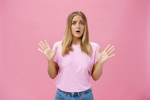 Woman looking nervous explaining with panicking gestures she not involved frowning opening mouth and gasping feeling concerned and worried waving hands over chest posing against pink wall. Copy space