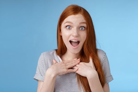 Amused happy grateful european redhead woman gasping drop jaw joyfully press palms chest thankful staring surprised incredible cool gift receive awesome proposal standing blue background.
