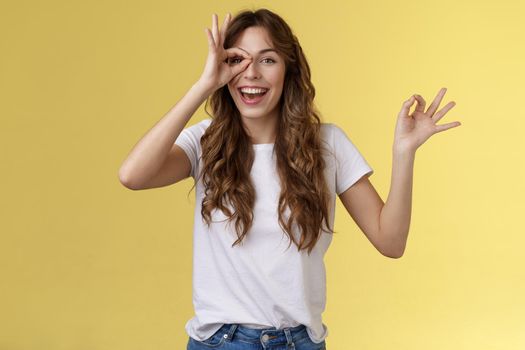 Friendly charismatic enthusiastic happy woman having perfect day show okay ok circle gesture look through ring amused wondered smiling broadly delighted express joy admiration yellow background. Lifestyle.