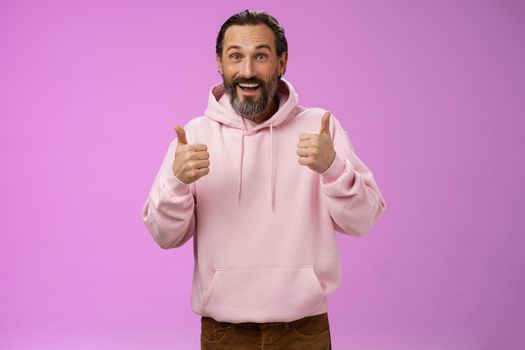 Energized supportive happy charming hipster mature guy bearded grey hair show thumbs up gesture yes approval sign totally agree cheering root for friend like awesome idea, standing purple background.