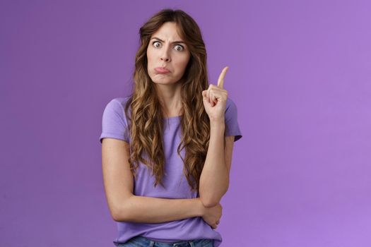 Strict funny curly-haired girl pulling disappointed angry face popping eyes stare camera shaking index finger disapproval scold bad behaviour stand serious bossy purple background.