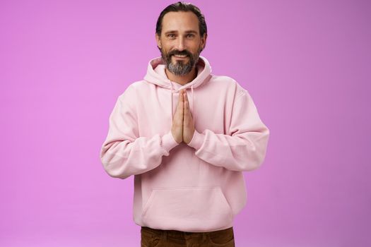 Peaceful attractive bearded mature mail model in trendy pink hoodie press palms together namaste praying gesture smiling delighted relaxed bowing buddhism faith, appreciating help, look thankful.